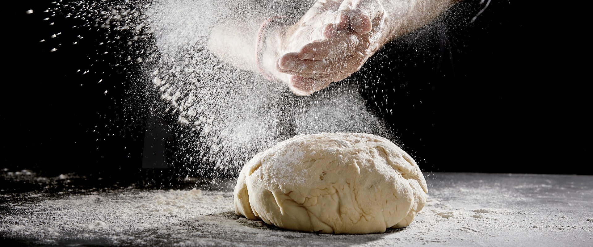 Chef scattering flour while kneading dough
