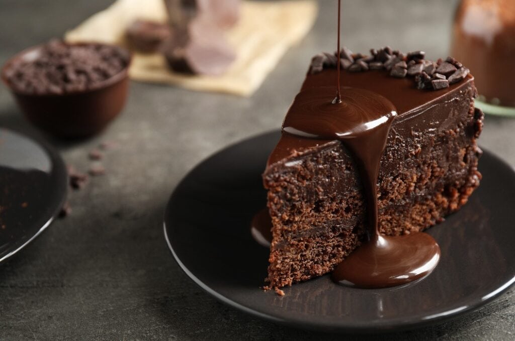 Pouring chocolate sauce onto delicious fresh cake on grey table, closeup